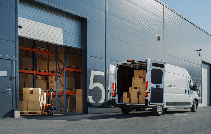 A sprinter van parked at a loading bay with boxes in the back and more boxes awaiting loading